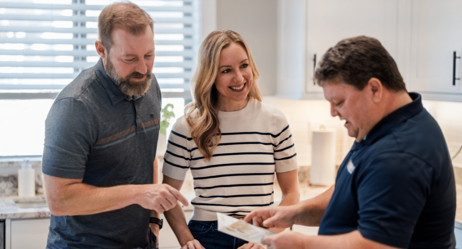 Male and female homeowners talk with HVAC service provider inside the kitchen of their home